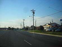 A divided highway approaching a signalized intersection with DE 24, which is marked on a small sign to the right of the roadway