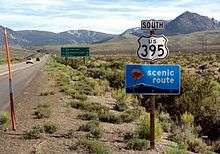 White sign in foreground saying "South US 395" and green sign in background giving distances to June Lake, Mammoth Lakes and Los Angeles.