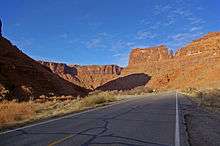 Highway following the right side of a narrow canyon with a long shadow cast from the left.