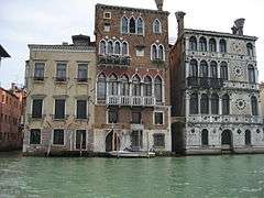 A row of three waterside Venetian buildings, having between three and five stories, with contrasting arrangements of arcades, windows and balconies.