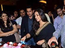 Actress Vidya Balan cuts a cake celebrating the success of Kahaani while actor Parambrata Chatterjee watches, along with several others.