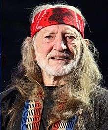 A face-shot of a Caucasian man with a red bandana, a white beard, and brown eyes