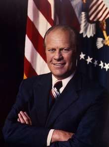 Ford, arms folded, in front of a United States flag and the Presidential seal.