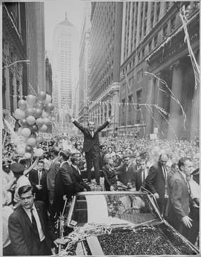 Nixon stands atop a motorcade vehicle, smiling, holding up his "v-sign" to a massive crowd on a Chicago street
